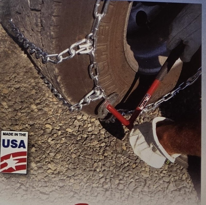 Gloved hand using a red chain tool with an orange tip on a tire chain on a truck tire